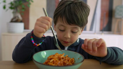 Young child twirling spaghetti on a fork with intense focus, showcasing concentration and determination during mealtime in a cozy home setting