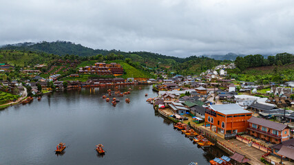 Aerial view of tranquil lakeside village nestled in lush, mist-covered hills under an overcast sky....