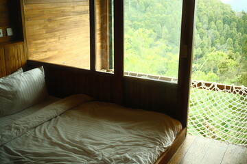Fototapeta premium A wooden cabin bedroom with a hammock by the window in the forested hills