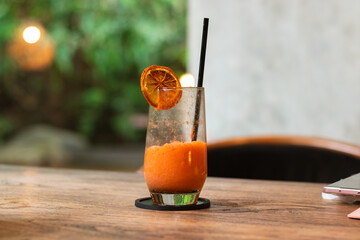 Mixed juice of orange and carrot, on a wooden table with garden background. After edits.