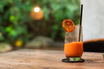 Mixed juice of orange and carrot, on a wooden table with garden background. After edits.