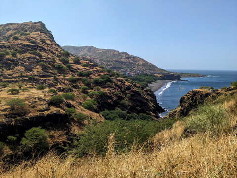 Rugged Coastline with Steep Golden Hills, Green Vegetation, and Curving Black Sand Beach Beside Blue Ocean