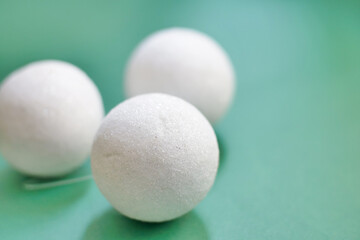 Close-up of three white decorative balls on a green background, minimal Christmas or winter holiday decoration