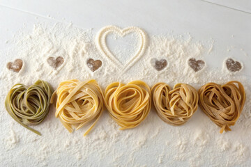 Heart-shaped pasta and noodles in assorted colors arranged neatly on flour-dusted surface