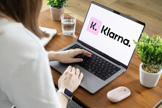 Poznan, Poland - August 23, 2025: Klarna logo prominently displayed on a laptop screen, as a woman actively types, showcasing modern digital payment and online shopping