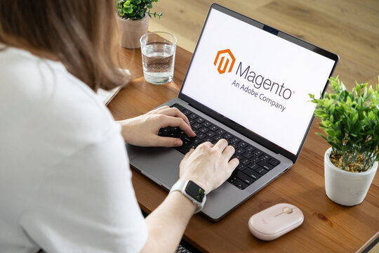 Poznan, Poland - August 23, 2025: Woman typing on a modern laptop, the Magento An Adobe Company logo prominently displayed on screen, symbolizing e-commerce development
