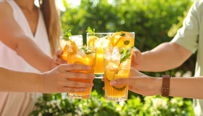 Refreshing iced tea with lemon and mint held by group of people celebrating outdoors in sunny garden