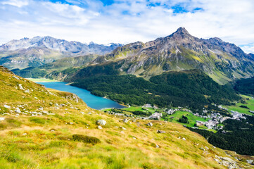 Panoramic view of Lake Sils, the village of Maloja, and the Maloja Pass, with the surrounding mountains, taken from above, in summer.