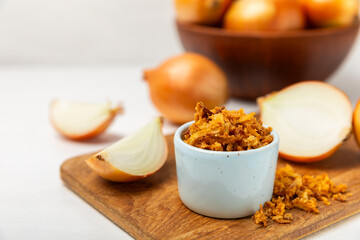 Crispy fried onions in a bowl on a wooden table. Roasted Onions. Seasoning for dishes. Spices. Salad dressing. Space for text. Copy space