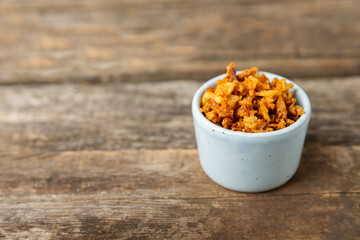 Crispy fried onions in a bowl on a wooden table. Roasted Onions. Seasoning for dishes. Spices. Salad dressing. Space for text. Copy space