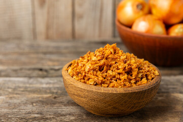 Crispy fried onions in a bowl on a wooden table. Roasted Onions. Seasoning for dishes. Spices. Salad dressing. Space for text. Copy space
