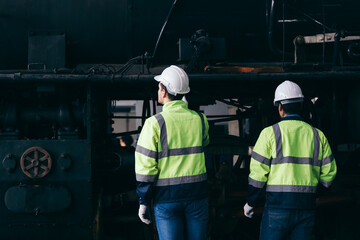 Two railway engineers wearing reflective safety jackets and helmets inspect an old locomotive...