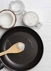Coconut oil and a frying pan on a wooden table close-up.. Vertical photo format 