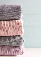 Warm knitted sweaters folded in a stack on a light background close-up.. Vertical photo format
