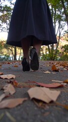 Woman walking on a paved path covered in autumn leaves
