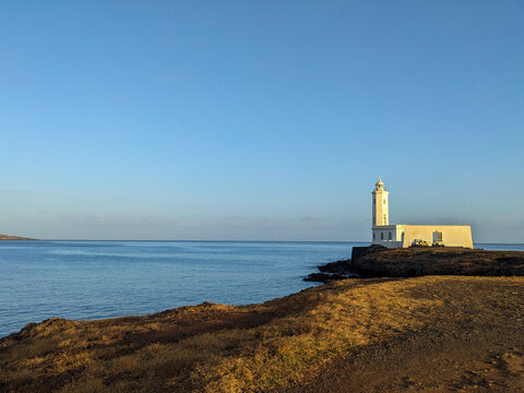 White Lighthouse on Rocky Coastline Beside Calm Blue Sea Under Clear Sky in Cape Verde, Africa