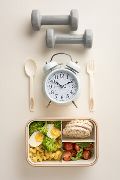 Neatly verticaly arranged fitness dumbbells, an alarm clock, utensils, and a meal preparation box promote healthy living