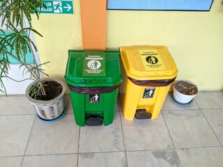 Green and yellow trash bins for organic and inorganic waste placed side by side indoors, promoting waste segregation and environmental cleanliness, with potted plants nearby.