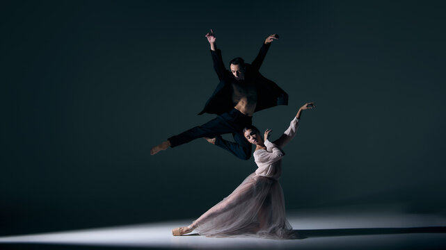 Male dancer soaring midair while female partner kneels in expressive pose. Concept of stage art, dramatic performance, passion, choreography, human connection and visual storytelling. - Powered by Adobe