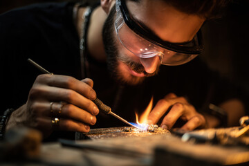 portrait of a jeweller in a modern workshop, wearing protective glasses, working with a small torch on a piece of jewellery,