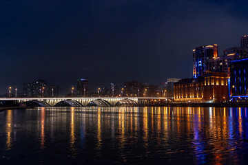 Panoramic view of the river in central Yekaterinburg with Bazhovsky Bridge in the distance. Cloudy sky and autumn or spring season create a moody atmosphere.