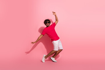 Young man in red t-shirt and white shorts enjoying a playful moment against a pink backdrop