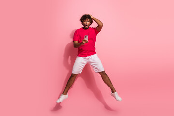 Young man in casual red shirt excited while using phone against pink background, capturing trendy...