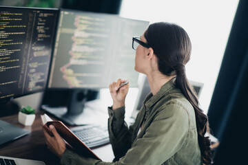 Charming programmer working remotely in a modern workspace while reviewing code on multiple screens and planning project tasks