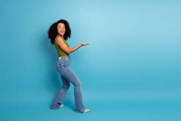 Joyful young woman with natural curls presenting with one hand on a vibrant blue background for lifestyle concept