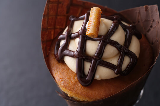 Close up of a cupcake with frosting chocolate drizzle and a caramel candy in a paper wrapper