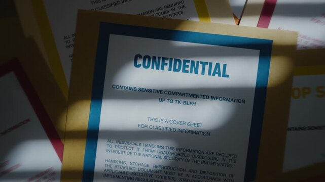 Manila file folder labeled confidential stacked on top of other classified files. Pile of various top secret folders and documents laid out on desk. Window shadow in dark office. Mystery and secrecy - Powered by Adobe