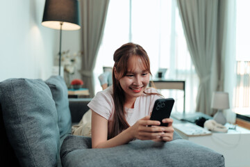 Young woman using smartphone while relaxing on sofa at home