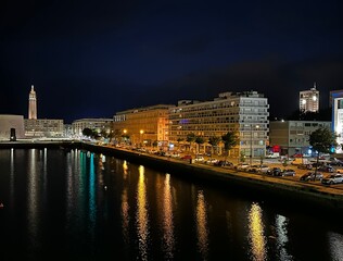 Fototapeta premium Nighttime cityscape with illuminated buildings reflecting in water, Le Havre, Normandy, France, July 2024