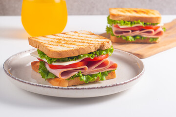 Close-up of two sandwiches with bacon, salami, prosciutto and fresh vegetables on rustic wooden cutting board. Club sandwich concept