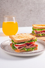 Close-up of two sandwiches with bacon, salami, prosciutto and fresh vegetables on rustic wooden cutting board. Club sandwich concept