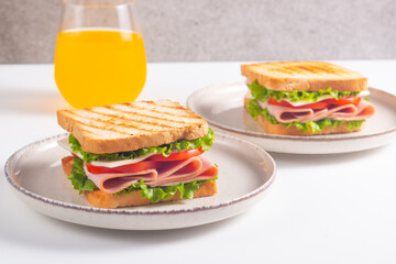 Close-up of two sandwiches with bacon, salami, prosciutto and fresh vegetables on rustic wooden cutting board. Club sandwich concept