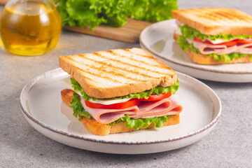 Close-up of two sandwiches with bacon, salami, prosciutto and fresh vegetables on rustic wooden cutting board. Club sandwich concept