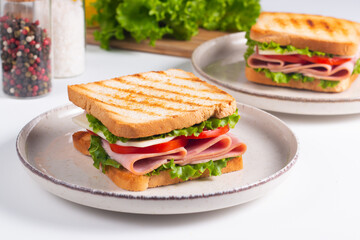 Close-up of two sandwiches with bacon, salami, prosciutto and fresh vegetables on rustic wooden cutting board. Club sandwich concept