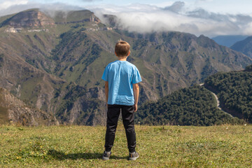 Rear view of boy standing against mountains and dramatic clouds in the sky