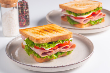 Close-up of two sandwiches with bacon, salami, prosciutto and fresh vegetables on rustic wooden cutting board. Club sandwich concept