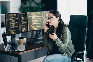 Young female programmer working on coding tasks at her desk in a modern workspace with multiple monitors.