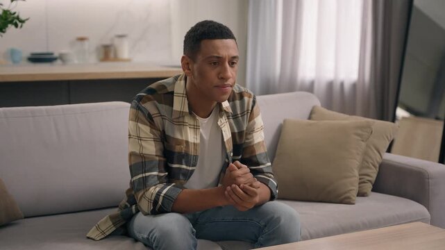 Upset sad frustrated African American man guy negative mood problem with mobile phone at home male confused disappointed thinking receive bank reject bad news finish stop using smartphone indoors