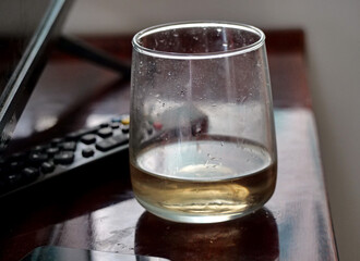 Glass of white wine - A Stemless Glass of White Wine Resting on a Dark Wooden Table near TV