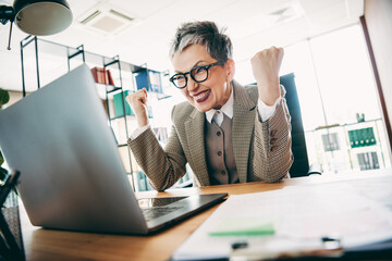 Mature businesswoman celebrating success at workplace, showcasing professional achievement and enthusiasm in a vibrant office
