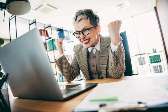 Mature businesswoman celebrating success at workplace, showcasing professional achievement and enthusiasm in a vibrant office