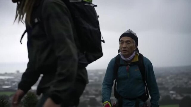 Three individuals stand together, possibly outdoors, wearing layered clothing, likely in a cold environment, with a cloudy sky overhead.