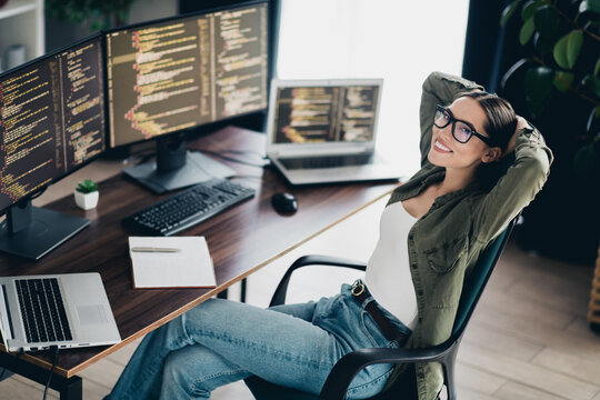 Charming female programmer enjoying a relaxing moment in her workspace surrounded by multiple monitors and coding projects