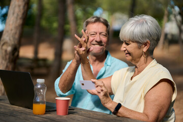 Senior couple making online payment with credit card in a park