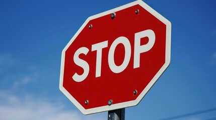 Obraz premium Bright red stop sign stands against a blue sky to ensure safe driving at the intersection during daytime