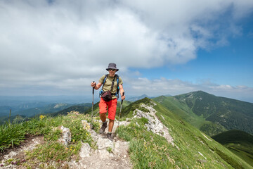 Fototapeta premium Hiker with trekking poles and backpack navigating rocky mountain trail on sunny day, scenic rolling green hills, capturing outdoor adventure and exploration, Mala Fatra Slovakia